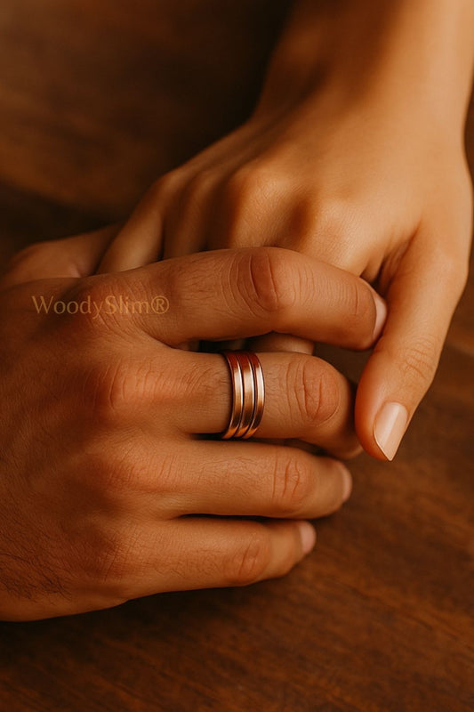 Bague bien-être en cuivre WoodySlim – mains d’un couple enlacées, bijou naturel sur table bois foncé, ambiance chaleureuse et minimaliste.