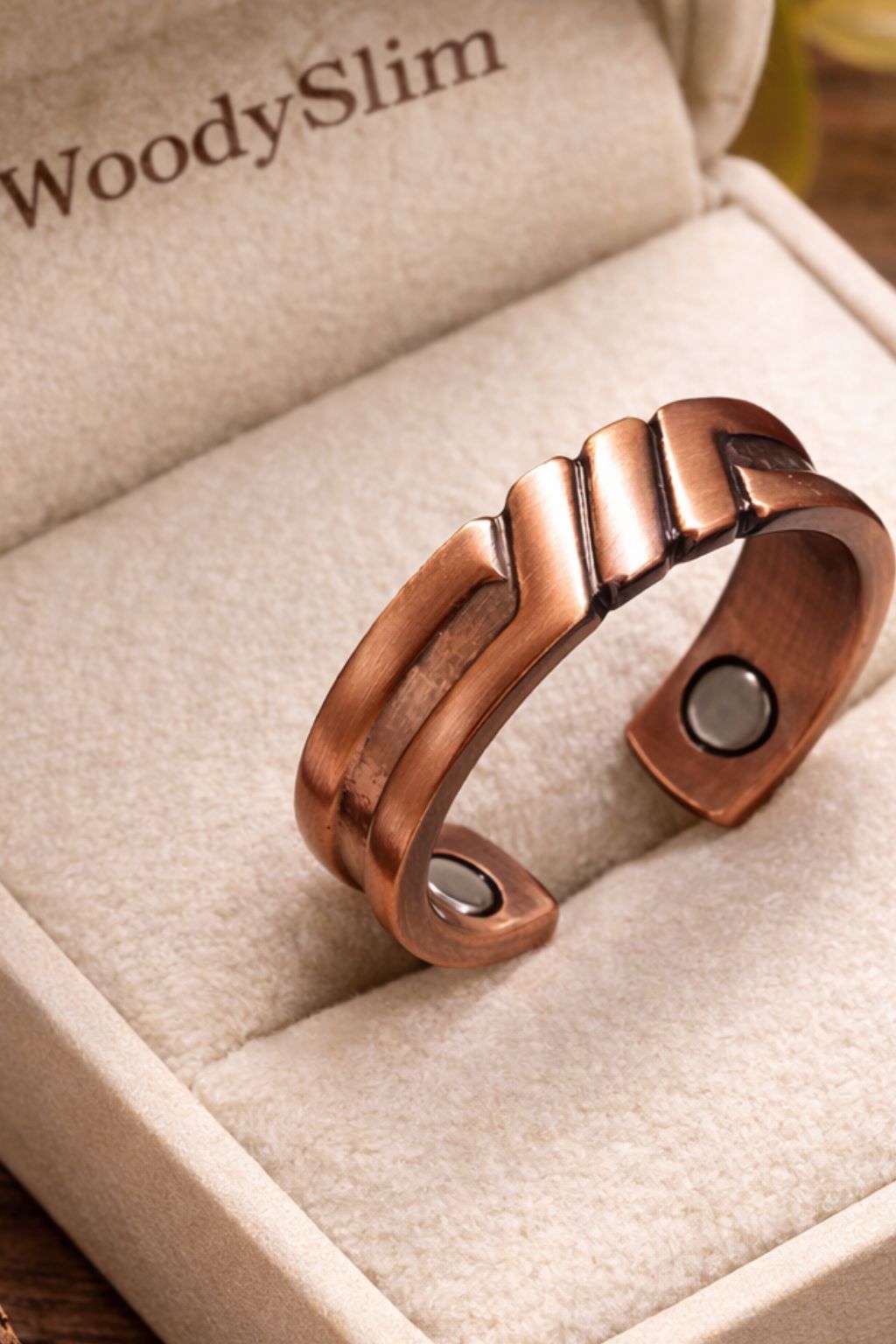 Bague ouverte en cuivre magnétique WoodySlim® posée dans un écrin beige avec logo WoodySlim, vue d’ensemble sur fond bois naturel, bijou bien-être au design épuré