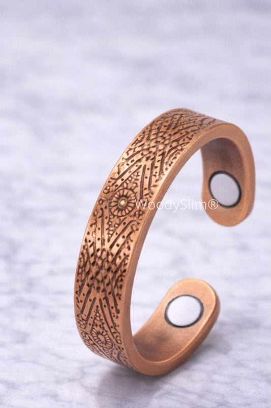 Bague magnétique en cuivre ouverte avec gravure artisanale bohème, posée sur fond marbre clair.