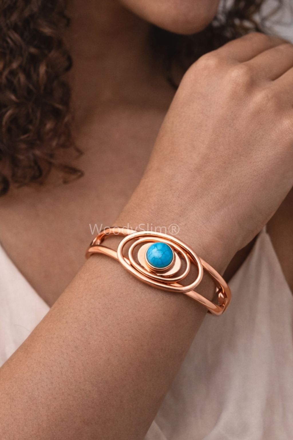 Bracelet cuivre WoodySlim® porté au poignet par une femme à la peau métisse, vêtue d’un top blanc crème. La pierre turquoise centrale et les spirales en cuivre ressortent en contraste subtil avec sa peau.