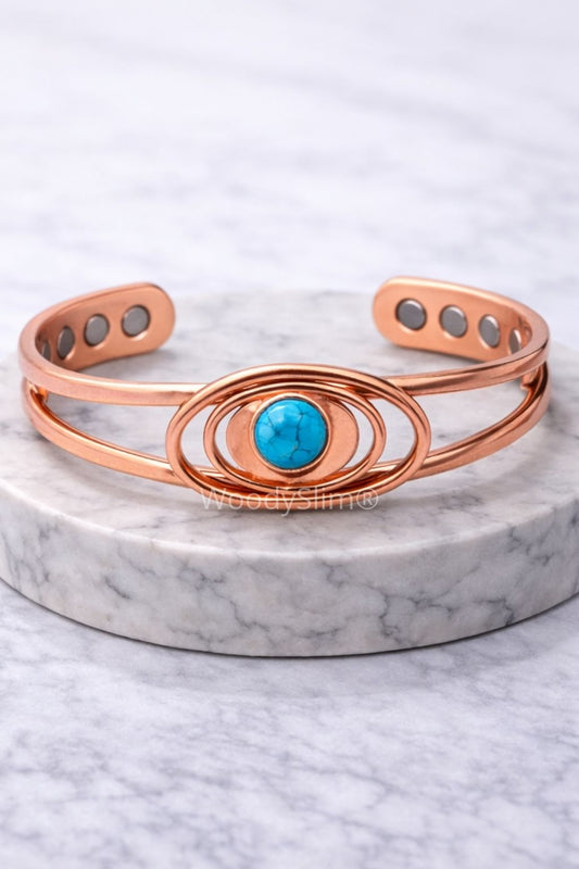 Bracelet rigide en cuivre poli, orné d’une pierre turquoise ronde centrale, entourée de cercles concentriques. Présenté sur un socle rond en marbre blanc, avec pastilles magnétiques visibles à l’intérieur.