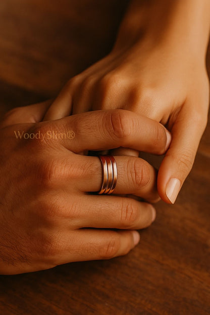 Bague bien-être en cuivre WoodySlim – mains d’un couple enlacées, bijou naturel sur table bois foncé, ambiance chaleureuse et minimaliste.