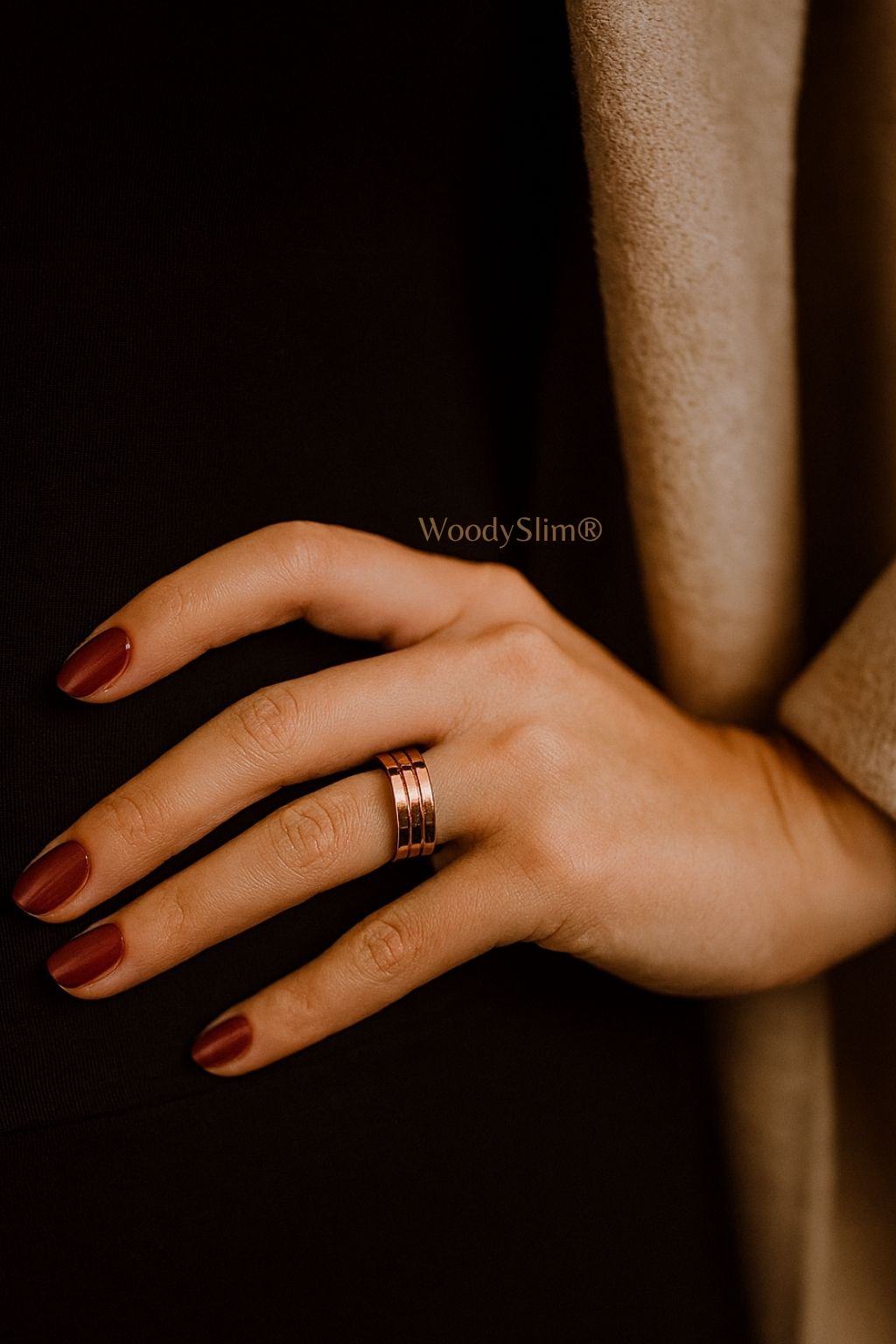 Bijou bien-être en cuivre WoodySlim – main de femme avec vernis foncé et bague triple anneau sur fond textile noir, atmosphère élégante et mystérieuse.