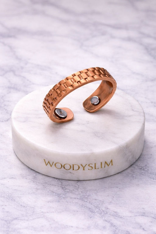 Vue de la bague magnétique en cuivre posée sur un socle en marbre blanc avec logo WoodySlim.