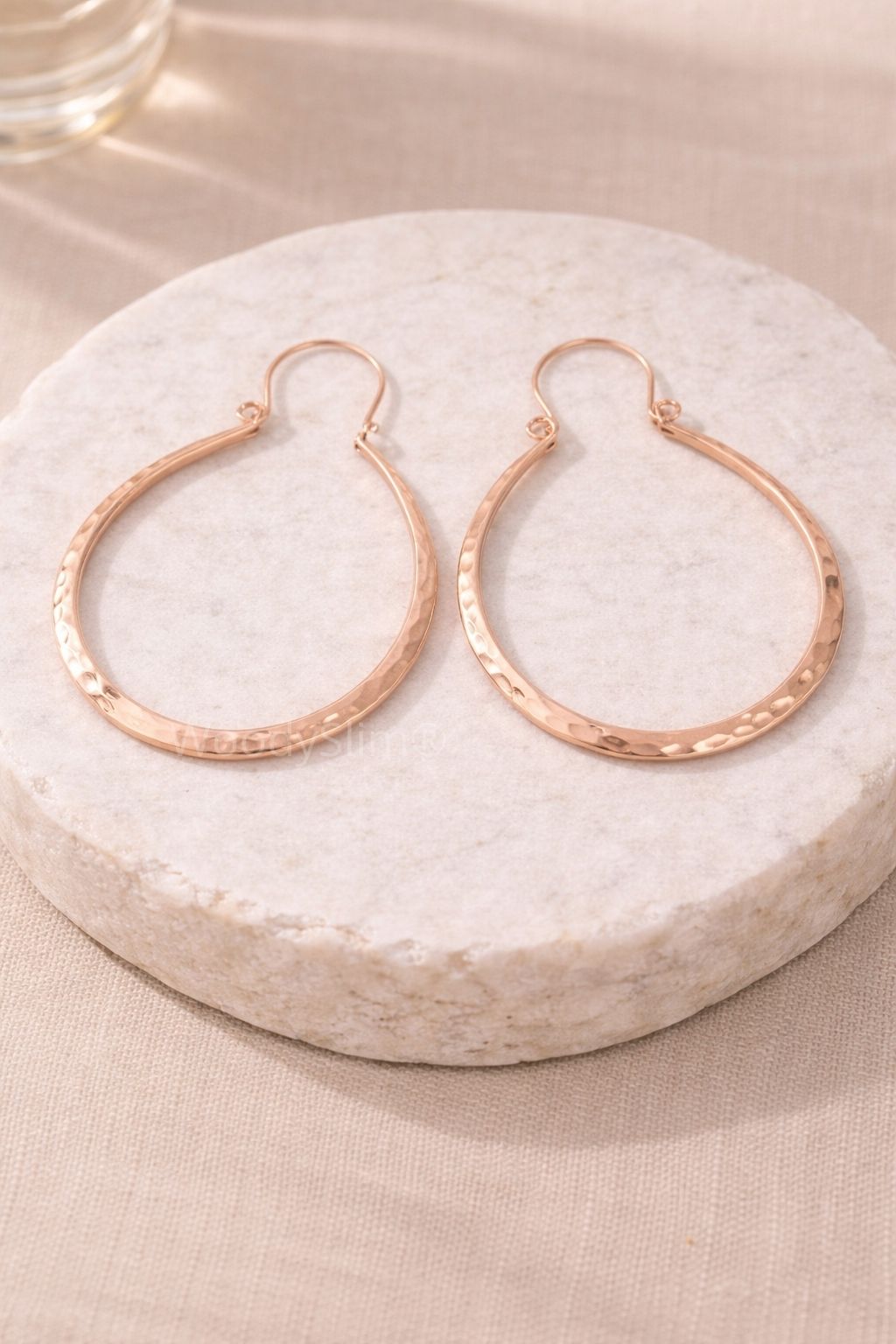 Paire de boucles d’oreilles créoles en cuivre martelé posées sur un socle clair, design circulaire et élégant, bijou WoodySlim.