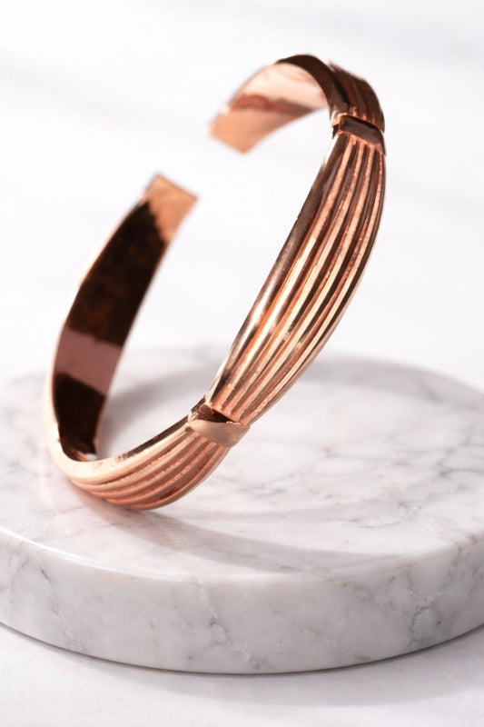 Bracelet WoodySlim en cuivre poli, présenté debout sur un socle rond en marbre blanc veiné. Fond clair, lumière douce et ambiance haut de gamme minimaliste.