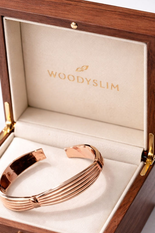 Bracelet rigide en cuivre rose posé dans un écrin WoodySlim en bois noble, avec intérieur crème et logo doré estampillé. Une mise en valeur premium parfaite pour offrir ou sublimer la marque.