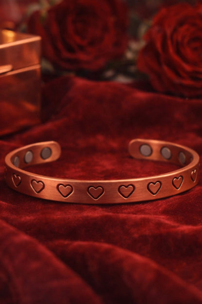 Bracelet en cuivre rigide ouvert avec motifs cœurs découpés et pastilles intérieures visibles, présenté sur tissu rouge, bijou WoodySlim.