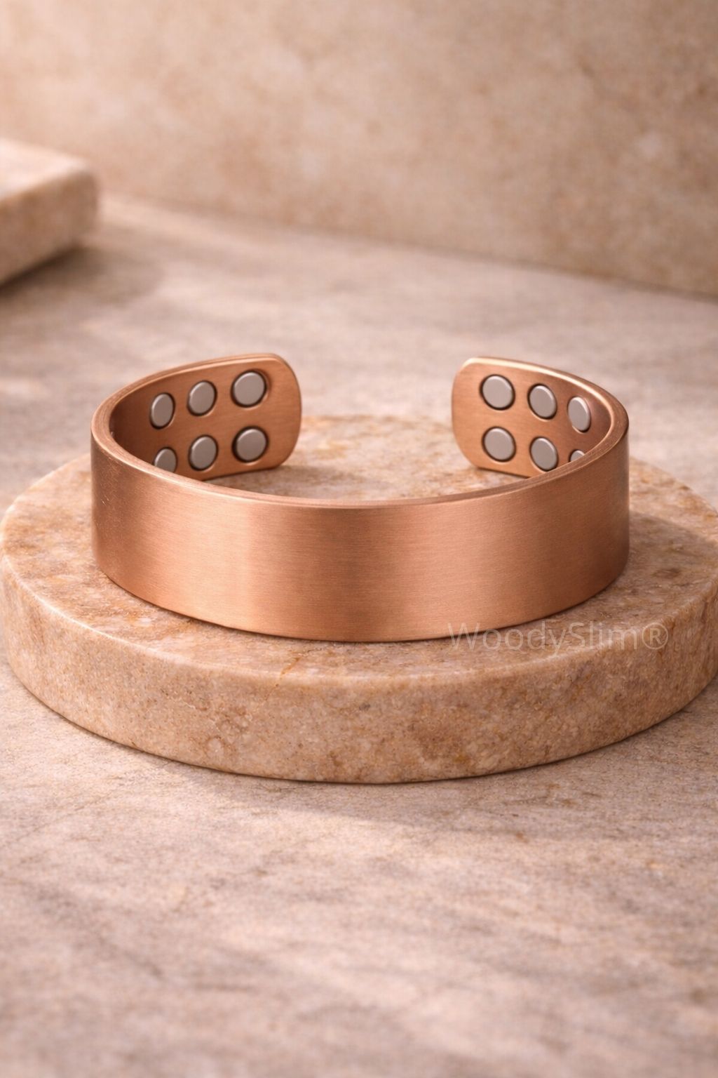 Bracelet manchette en cuivre mat large avec six aimants de chaque côté, posé sur un socle marbré cuivré, bijou magnétique haut de gamme WoodySlim.