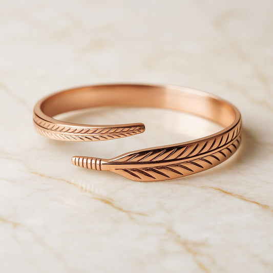 Bracelet ouvert en cuivre avec gravure en forme de feuille, posé sur un fond marbré clair, bijou élégant pour femme dans un style naturel