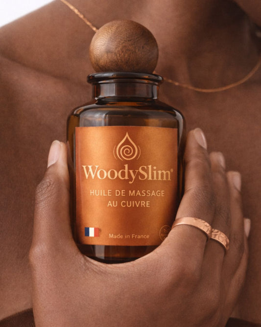 Huile de massage au cuivre WoodySlim tenue en main avec flacon ambré Made in France.