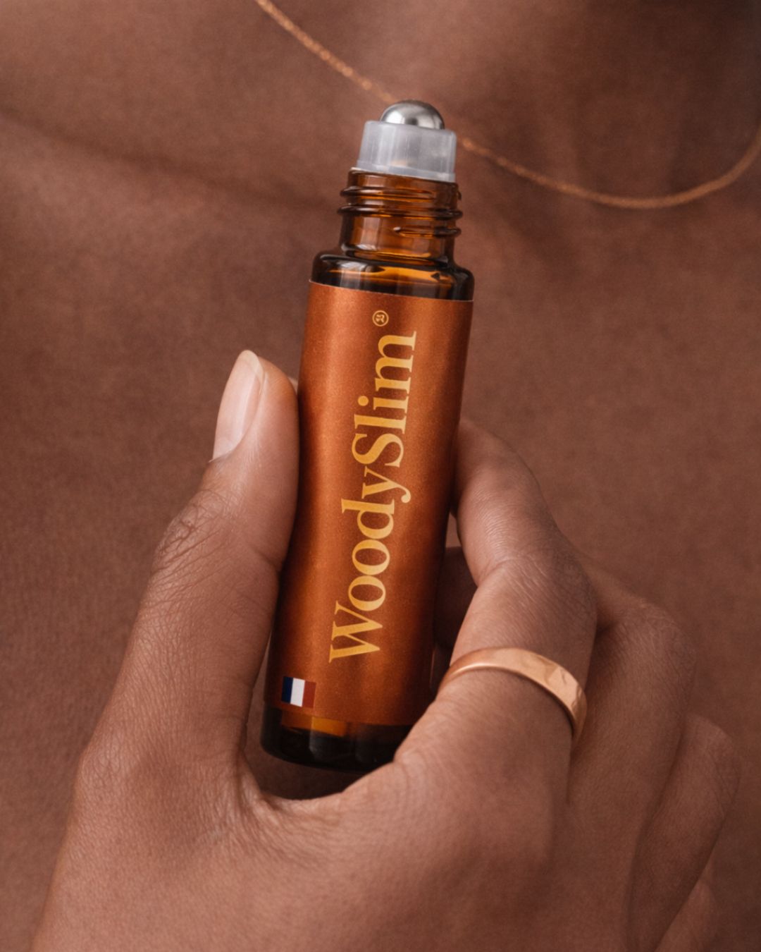 Roll-on WoodySlim à l’huile de rituel au cuivre tenu en main avec bijou en cuivre.