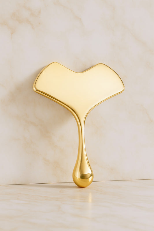 Outil de massage facial en cuivre doré posé sur fond marbré clair pour routine beauté anti-âge